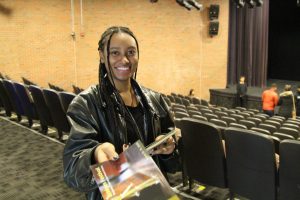 A volunteer usher handing a program to you as you enter the theatre to watch a show during Bridges Festival in March Break produced by a professional theatre company